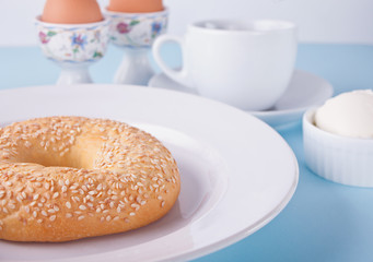 Fresh healthy bagel on a white plate with cup of coffee, cream cheese and eggs for breakfast