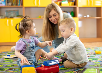 Babysitter plays with babies in nursery or kindergarten