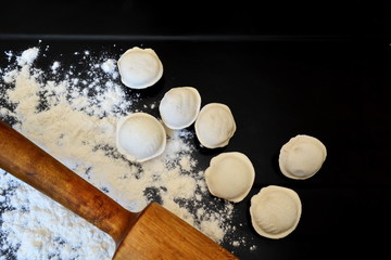 raw homemade handmade forcemeat dumplings, rolling pin and white wheat flour on the kitchen black table