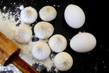 raw homemade handmade forcemeat big dumplings, rolling pin, chicken eggs and white wheat flour on the kitchen black table