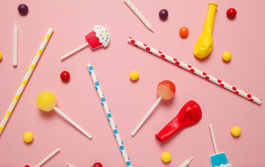 Children's cheerful decor for a party, pink background. Sweet candies, bright balls, festive candles and straws.