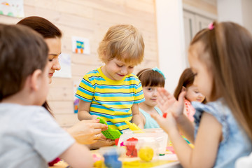 Obraz na płótnie Canvas Teacher teaches kids modeling clay in playroom at daycare or kindergarten