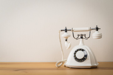  old white telephone on wooden table with color wall background