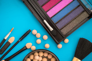 Top, up view of professional cosmetics, makeup background. Brushes, eye shadows, eyebrow pencils, powder, bronzing balls, mascara, red lipstick. Tools isolated on blue. Concept of get ready for party