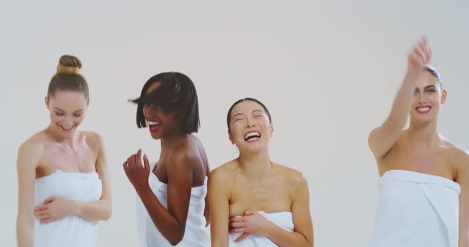 Slow motion of beautiful young smiling women of different ethnicities with perfect firm and slim body in white bathing towels dancing and having fun isolated on white background.