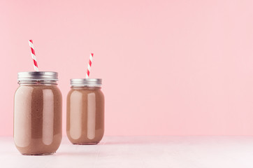 Healthy fresh chocolate smoothie in two jars with  striped straws, silver caps on pastel pink background, copy space.