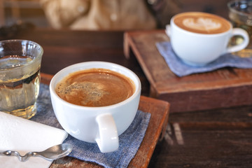 Closeup image of two white cups of hot coffee and a glass of tea on vintage wooden table in cafe
