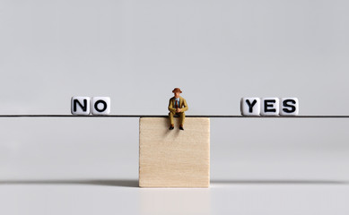 A miniature businessman sitting between the NO text white cube and the YES text white cube on a...