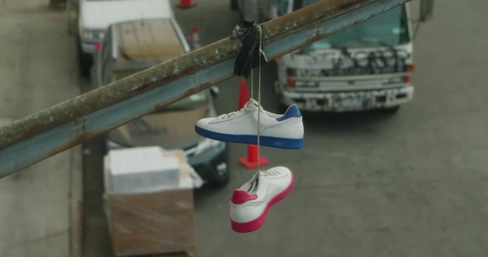 Generic white sneakers hanging from street light pole on gritty urban street, seen high angle from above.