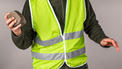 Rebel or protesting worker in a yellow vest with a brick in his hands on a gray background