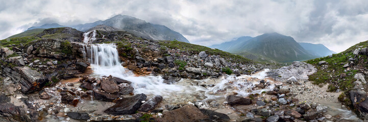 Mountain waterfall stream in misty rainy weather in the valley flowers. Cylindrical panorama 360