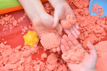 Children play with pink kinetic sand for sculpting figures. Top view, hands close up