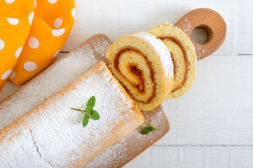 Delicious biscuit roll with apricot jam and powdered sugar on a white wooden table. Dessert for breakfast. Top view.