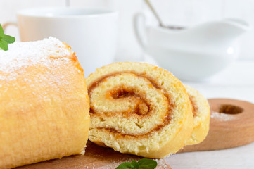 Delicious biscuit roll with apricot jam and a cup of tea on a white wooden table. Dessert for breakfast. Copy space
