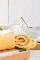 Delicious biscuit roll with apricot jam and a cup of tea on a white wooden table. Dessert for breakfast. Copy space