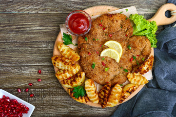 Large schnitzel with baked golden potatoes on a wooden cutting board. Wiener Schnitzel. Top view.