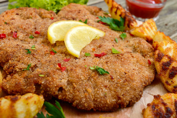 Large schnitzel with baked golden potatoes on a wooden cutting board. Wiener Schnitzel.