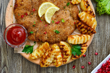 Large schnitzel with baked golden potatoes on a wooden cutting board. Wiener Schnitzel. Top view.