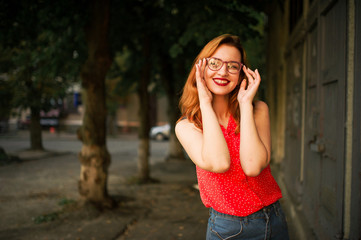 Attractive redhaired woman in eyeglasses, wear on red blouse and jeans skirt posing.