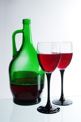 Two glasses of red wine and a green bottle on a light background.