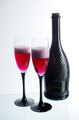 Two glasses of red champagne and a dark bottle on a light background.