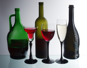 Three bottles and three glasses of wine on a light background.