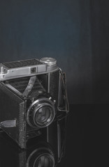 Zabytkowy, bardzo stary aparat fotograficzny z wysuwanym obiektywem na czarnam, lustrzanym blacie.