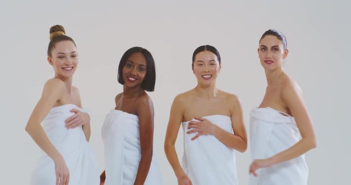 Slow motion of beautiful young smiling women of different ethnicities with perfect firm and slim body in white bathing towels dancing and having fun isolated on white background. 