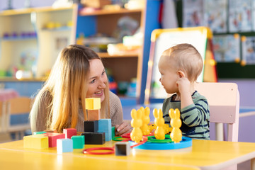 Kid and kindergarten teacher play with colorful wooden block toys on table - 256587782