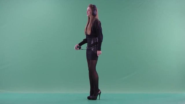 Young beautiful woman in black casual clothes is listening to music and dancing standing sideways in front of on green screen