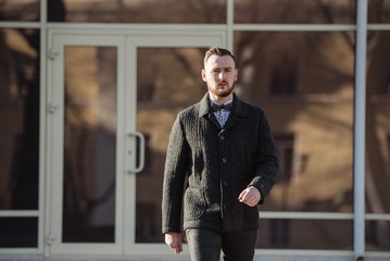 A man in a suit and sweater poses on the street. Advertising of men's clothing