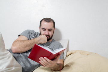 Young man pensive reads a book in the bedroom. White background.