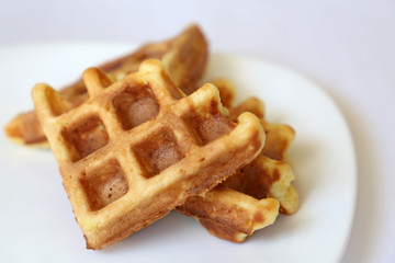 Belgian waffles in white plate. Healthy breakfast close up, pieces of freshly baked classic wafer