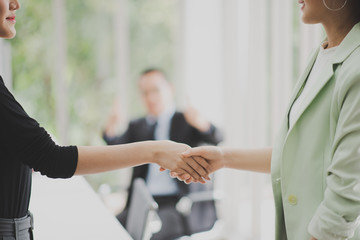 Obraz premium Closed up of business woman shaking hands which standing in front of business man who sitting on the chair at the working place or meeting room.