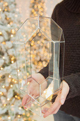 Girl holding glass vase near christmas tree with lights. Abstract geometric shape of glass.