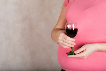 Young pregnant woman keeps a  glass of red wine. Closeup