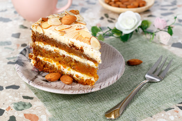 Close-up the piece of vegetarian carrot cake with almonds on a saucer and a fork near. Pink cup and plate with almonds in the background.