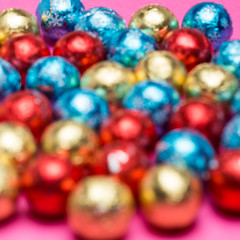 Blurry round chocolate candies in a multi-colored foil on a pink background