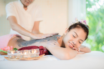 Young Asian woman receiving mud therapy massage in spa salon, Hand putting mud scrub on female back, Spa concept.