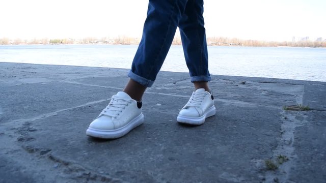 View of white sneakers and jeans on the background of concrete slabs in the city.