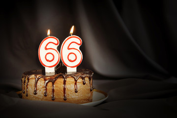 Sixty six years anniversary. Birthday chocolate cake with white burning candles in the form of...