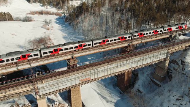 Aerial Shot top shot of a train crossing a bridge over the mountain river in sunny winter day.