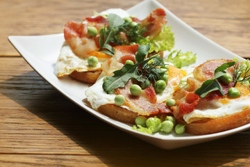 Bruschetta with rucola, chrispy bacon and poached egg served on white plate