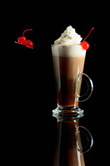 Layered coffee cocktail with whipped cream and red cherry.