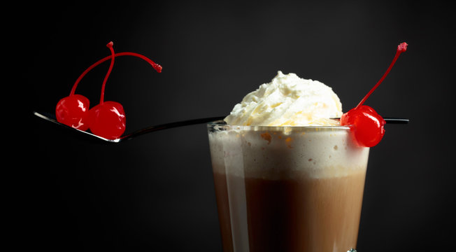 Layered coffee cocktail with whipped cream and red cherry.