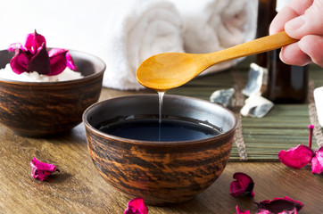 Closeup of oil for massage in the bowl and other cosmetic products. Woman preparing and pouring cosmetic oil for beauty procedures