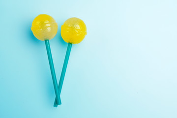 Two big bright yellow tasty lollipops on green sticks on blue pastel background. Lollipops concept. Copy space for text.