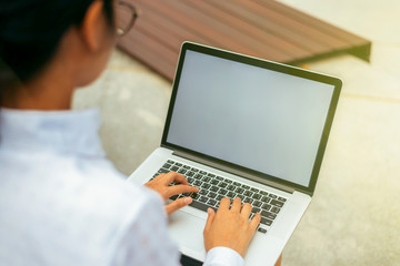 Businesswoman wearing glasses from behind view typing laptop keyboard on her lap with blank space...
