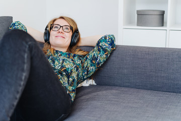 Obraz premium Happy young woman listening to music on a sofa