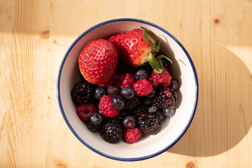 Bowl of fresh berries: strawberries, blueberries, raspberries and blackberries; natural morning light, wooden background. Healthy eating